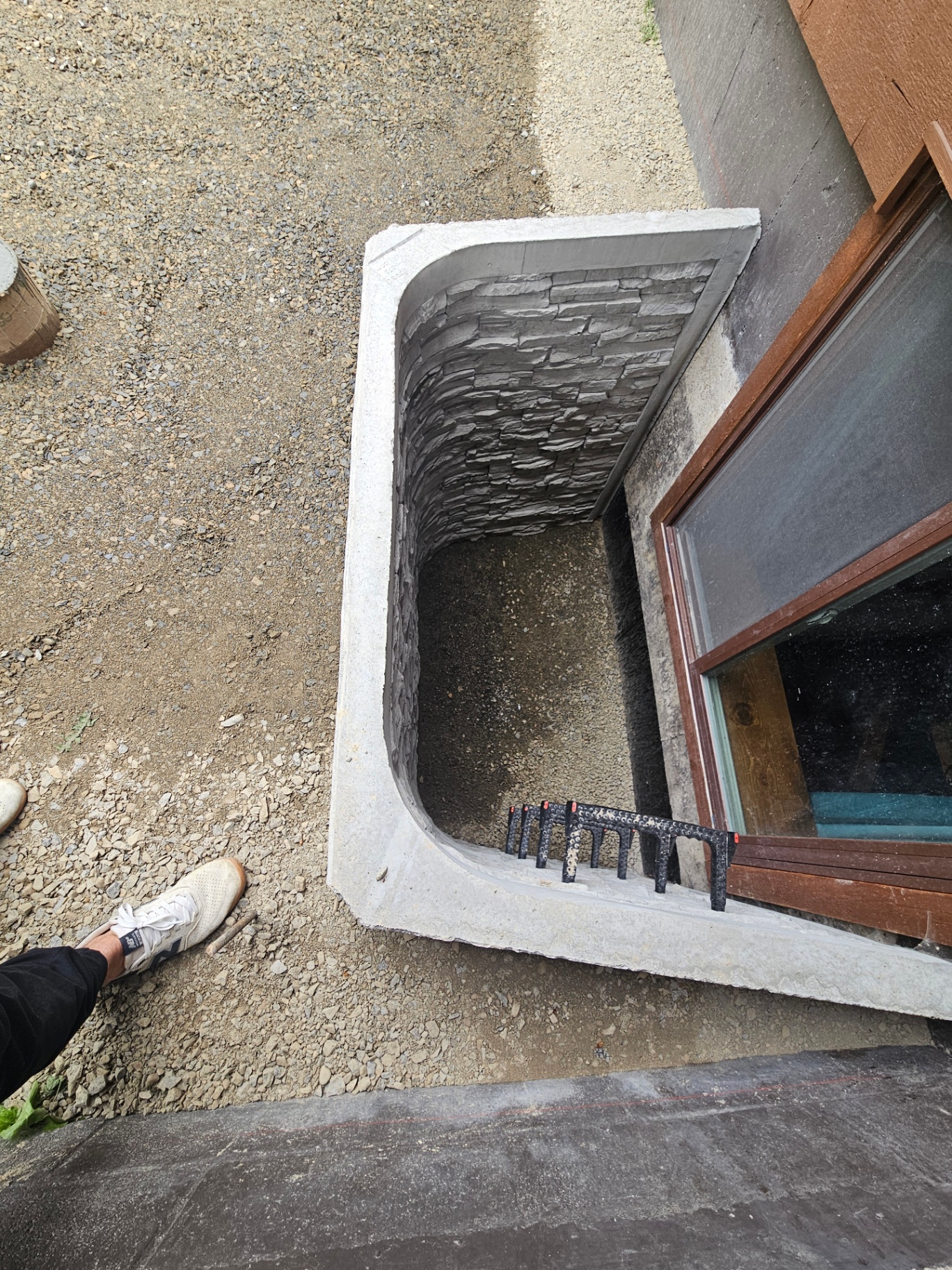 Curved concrete egress window well with stacked-stone liner and ladder